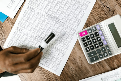 A close-up of a person pointing at financial documents with a marker, accompanied by a calculator, symbolizing financial planning and debt management.