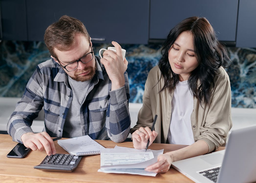 A couple sits at a table, examining financial documents and using a calculator, indicating a review of their financial situation.