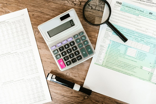 Calculator, magnifying glass, and tax forms on a wooden desk.