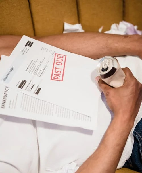 A person holding a can while surrounded by documents, including a past-due notice, highlighting financial struggles.