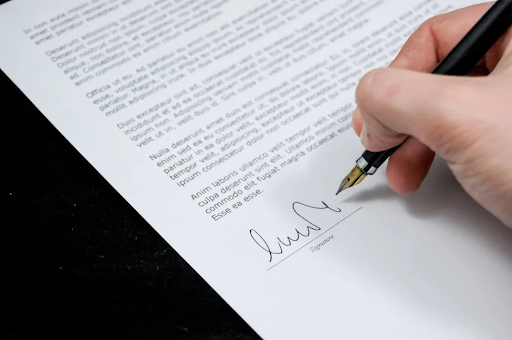 A person signing a document with a fountain pen, symbolizing the formal process of writing and sending a cease and desist letter.