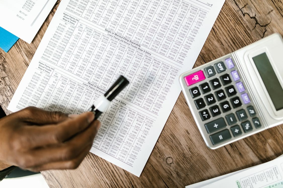 Hand holding a marker over a financial document with a calculator nearby on a wooden table.