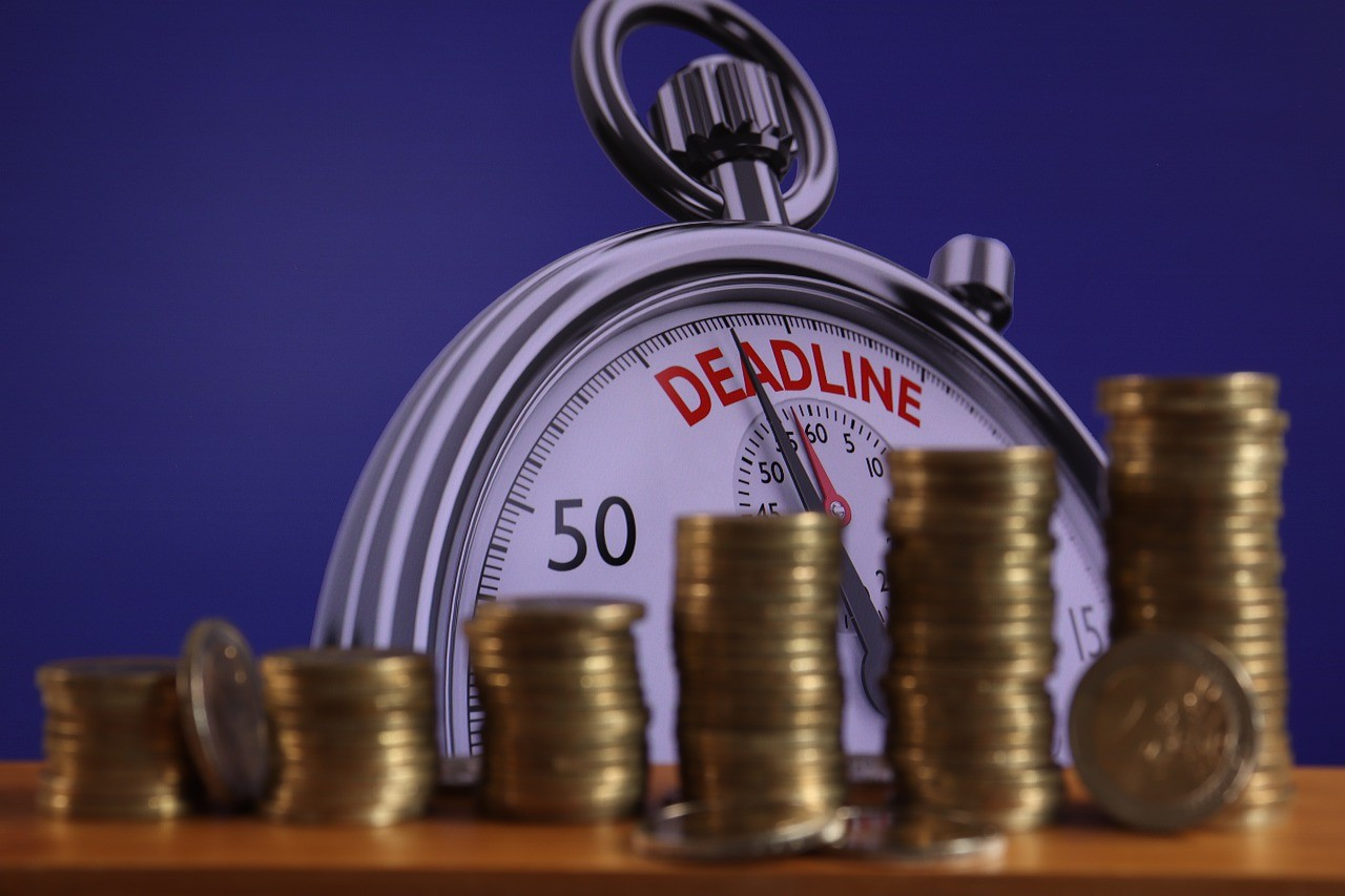 Stacks of coins in front of a stopwatch with the word "Deadline," emphasizing the urgent need to address credit card debt issues.