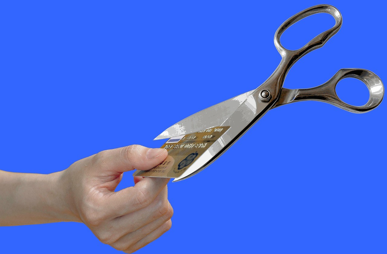 A hand using scissors to cut a credit card, representing the concept of credit card debt consolidation.