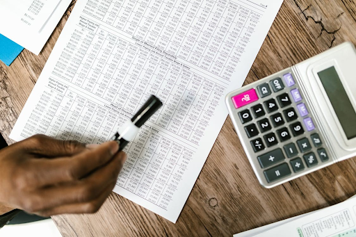 Close-up of a hand holding a marker, pointing at a financial document with a calculator on the table, representing the detailed work involved in debt relief planning.