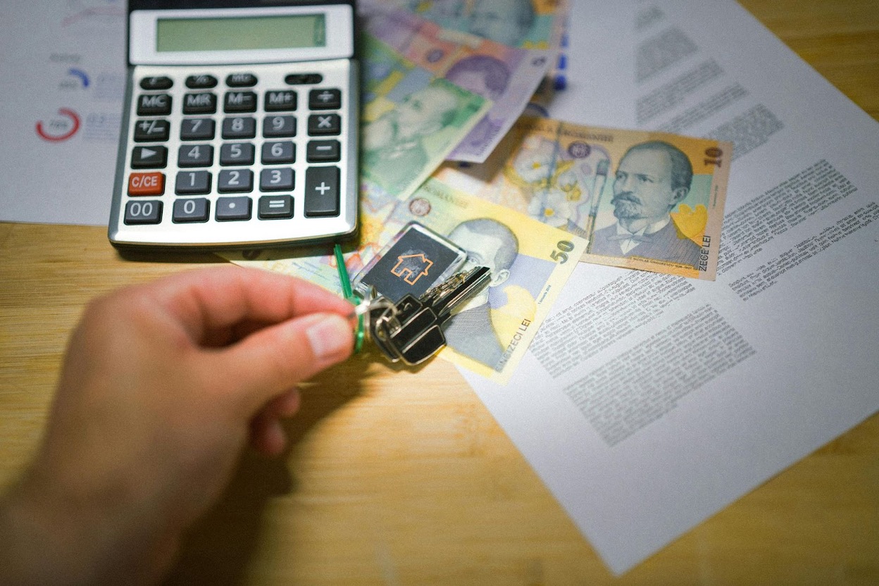 A hand holding house keys, calculator, and financial documents with money.