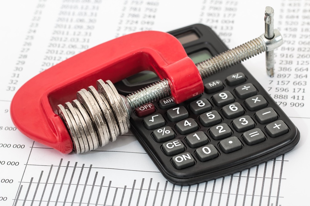 Coins clamped in a vice over a calculator symbolizing financial pressure